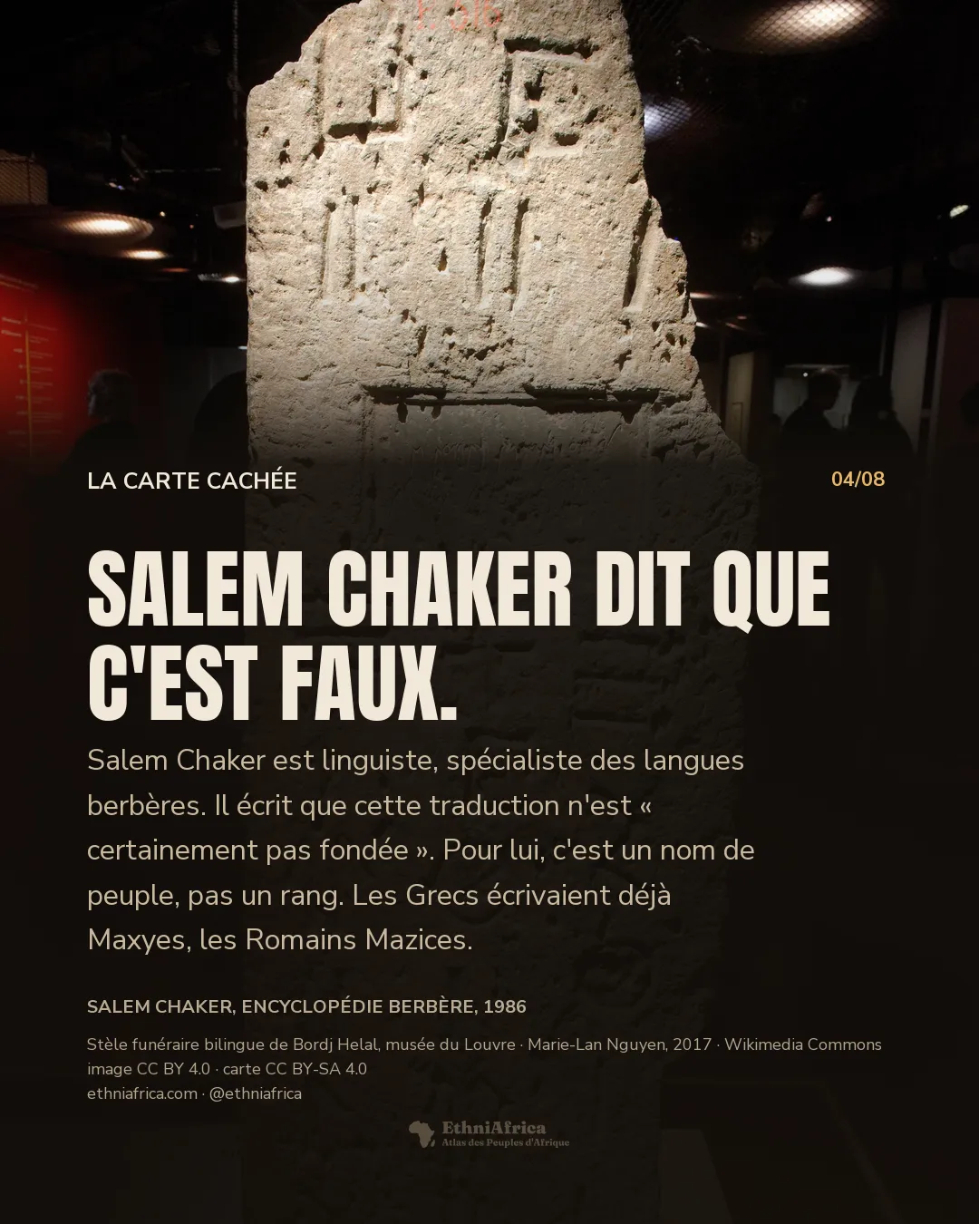 une haute stèle de pierre dressée dans une vitrine de musée, couverte de signes incisés, avec un cartouche rectangulaire gravé en son milieu