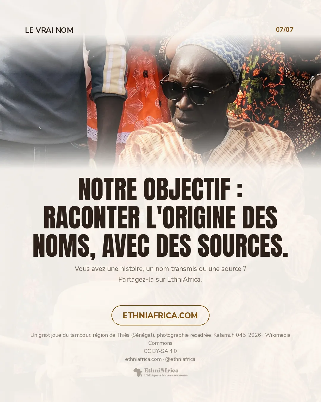 un griot âgé, lunettes noires et bonnet brodé, frappe un grand tambour avec une baguette ; derrière lui, des vêtements et des mains qui applaudissent