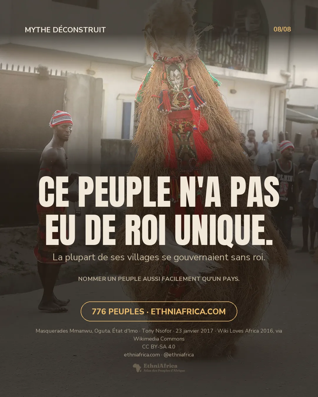 deux masquerades de raphia et de tissu rouge dansent l'une derrière l'autre dans une rue, devant des spectateurs alignés le long des façades